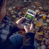 Meisje kijkt op iPhone naar Natuurwijzer met jas in de herfst