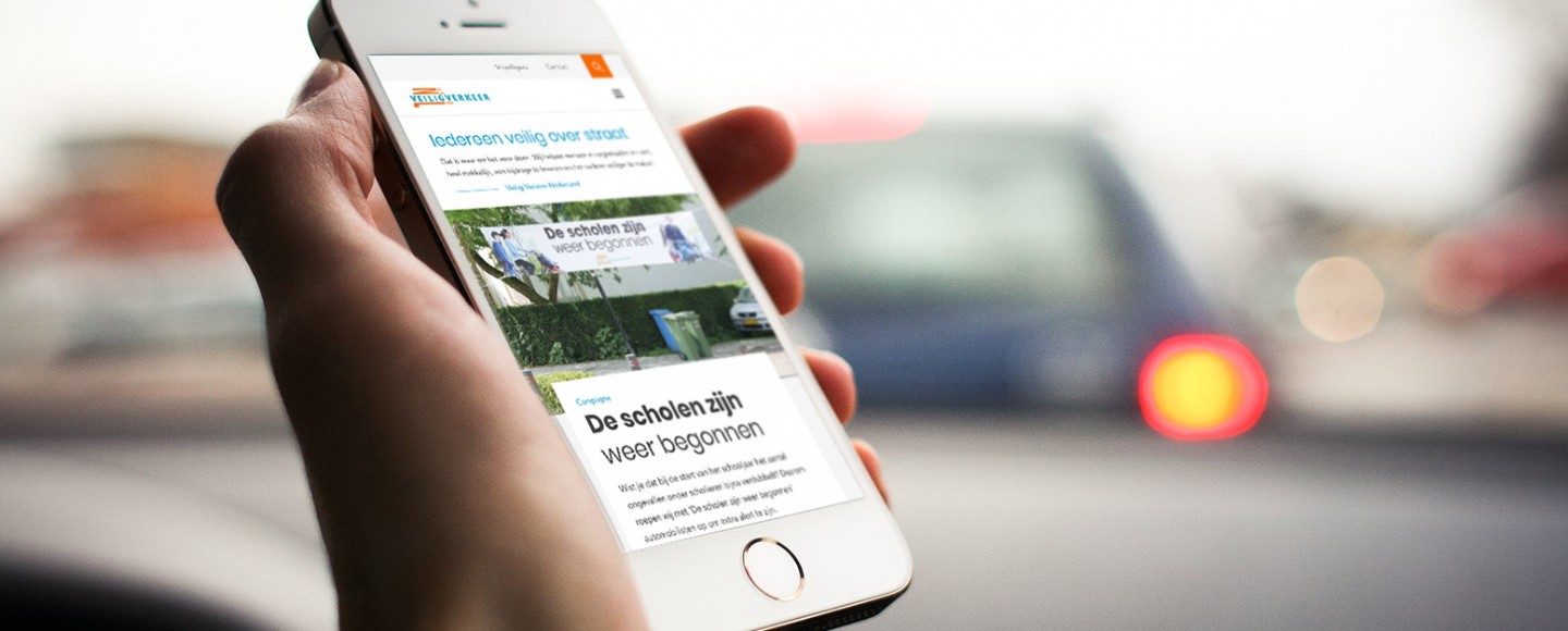 iPhone met website van Veilig Verkeer Nederland en auto door de voorruit op de achtergrond